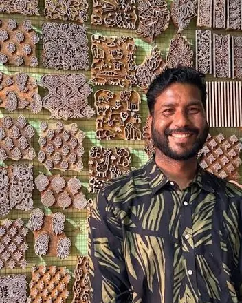Deepak Chhipa in front of a wall of carved printing blocks.