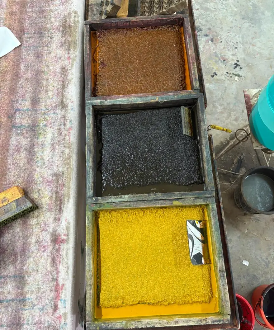 Three shallow trays of dye on a worktop, one brown, one near-black, one yellow.